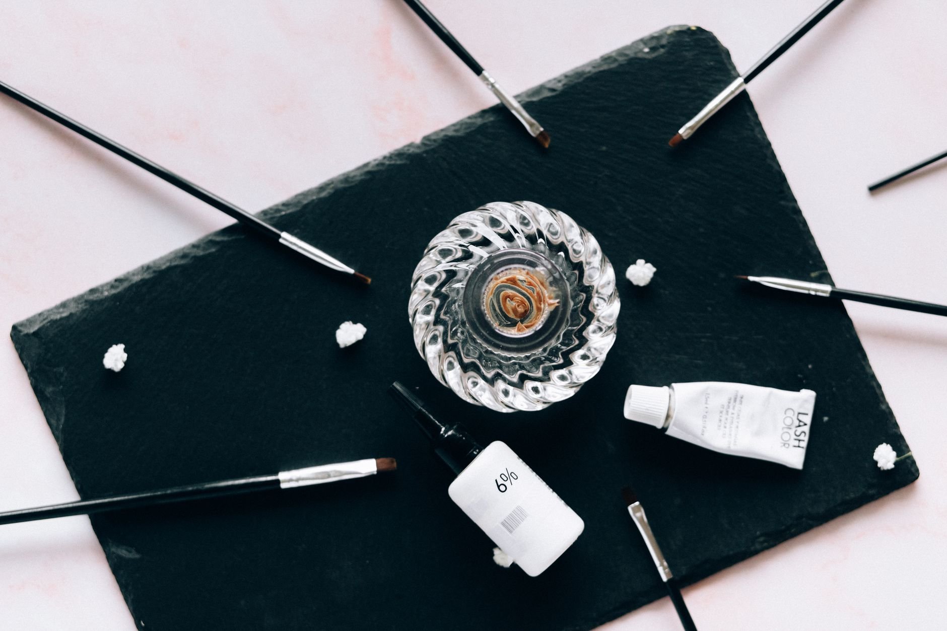 Cosmetic products and makeup brushes arranged on a dark slate surface
